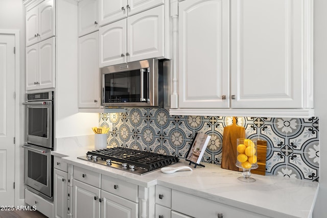 kitchen with light stone countertops, appliances with stainless steel finishes, white cabinets, and decorative backsplash