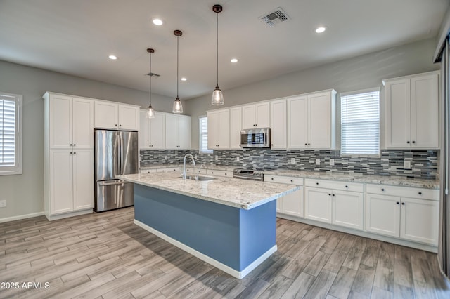 kitchen featuring white cabinets, stainless steel appliances, an island with sink, sink, and hanging light fixtures