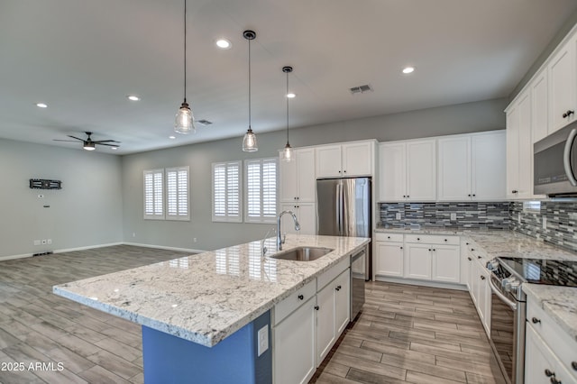 kitchen featuring appliances with stainless steel finishes, white cabinetry, an island with sink, sink, and ceiling fan