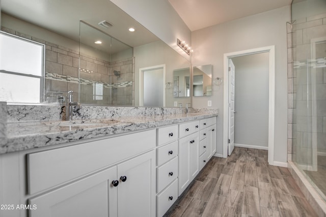 bathroom with wood-type flooring, tiled shower, and vanity