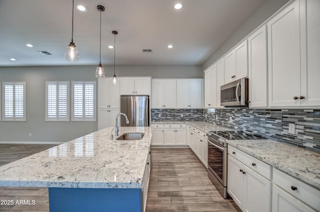 kitchen featuring appliances with stainless steel finishes, a kitchen island with sink, white cabinets, and sink