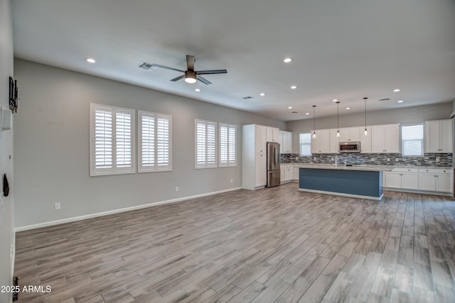 kitchen featuring ceiling fan, appliances with stainless steel finishes, hanging light fixtures, a kitchen island, and white cabinets