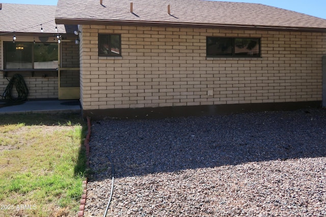 view of home's exterior with a shingled roof and brick siding