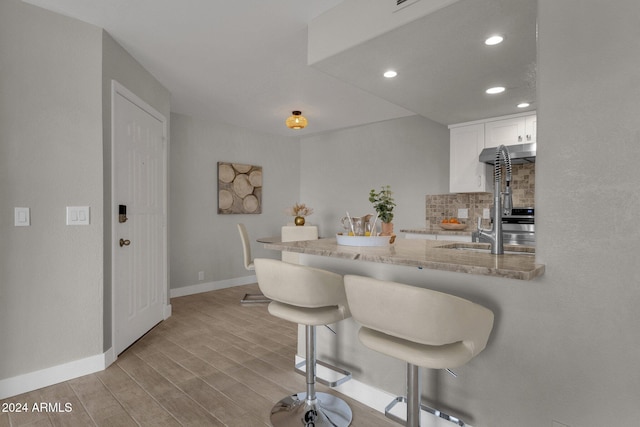 kitchen featuring light hardwood / wood-style flooring, white cabinetry, backsplash, light stone countertops, and a kitchen bar