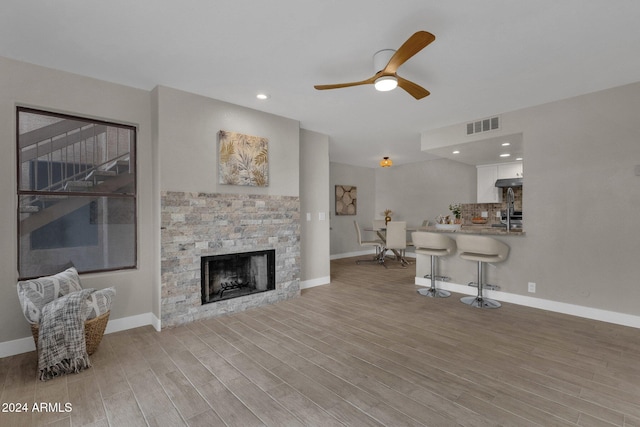 living room with a fireplace, ceiling fan, and light wood-type flooring