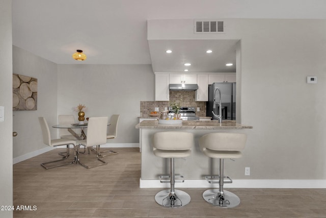 kitchen with a breakfast bar, appliances with stainless steel finishes, kitchen peninsula, decorative backsplash, and white cabinets