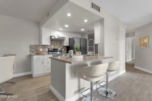 kitchen with a breakfast bar, white cabinets, light wood-type flooring, and appliances with stainless steel finishes