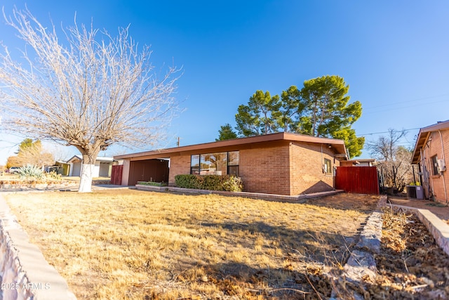 view of front of house with cooling unit, brick siding, and a front lawn