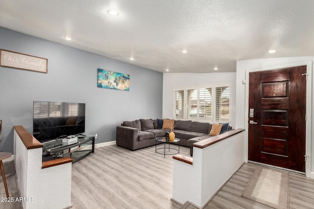 living room featuring a textured ceiling, light wood-type flooring, baseboards, and recessed lighting