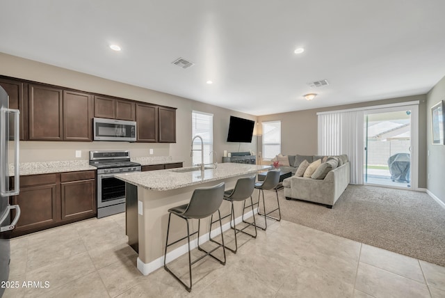 38150 W San Sisto Ave, Maricopa, AZ 85138 - kitchen with appliances with stainless steel finishes, a sink, a breakfast bar, open floor plan, and dark brown cabinetry