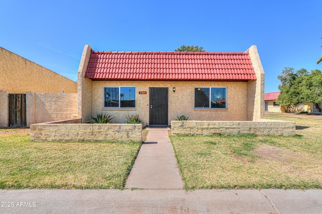 view of front of house with a tiled roof, a front yard, and stucco siding