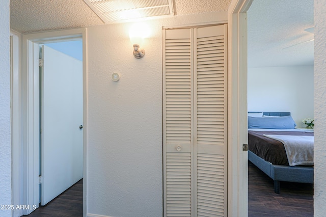 hallway featuring dark wood-style flooring, visible vents, a textured wall, and a textured ceiling