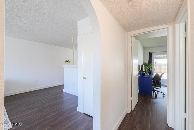 corridor with arched walkways, dark wood-type flooring, a textured ceiling, and baseboards