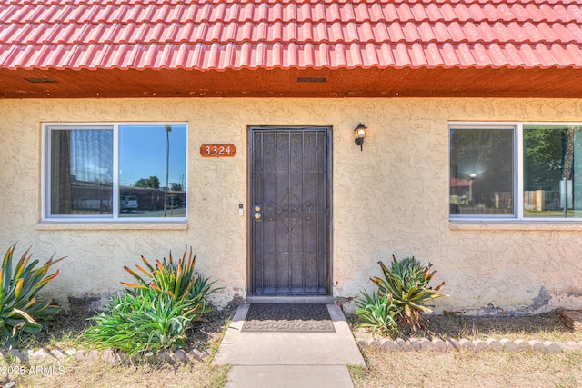 property entrance featuring a tile roof and stucco siding