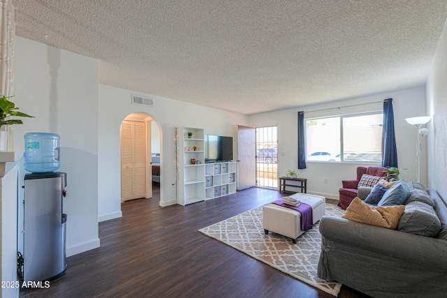 living area featuring dark wood-style floors, arched walkways, visible vents, and baseboards