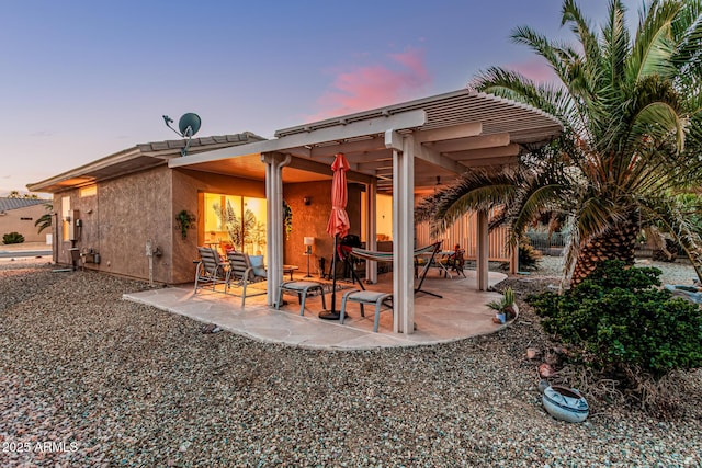 back of property at dusk with a patio and stucco siding