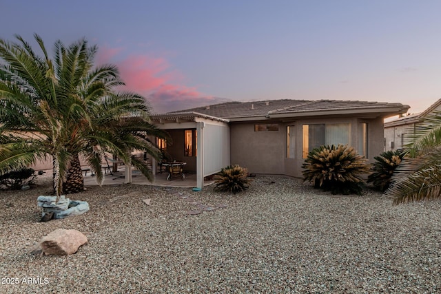 rear view of property with stucco siding, a tiled roof, and a patio