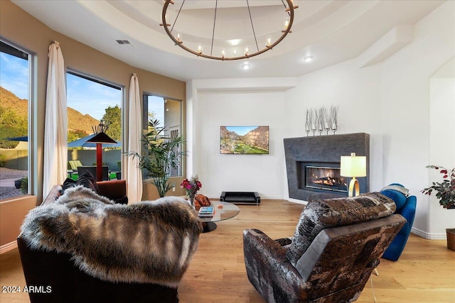 living room featuring an inviting chandelier, a tray ceiling, and light wood-type flooring