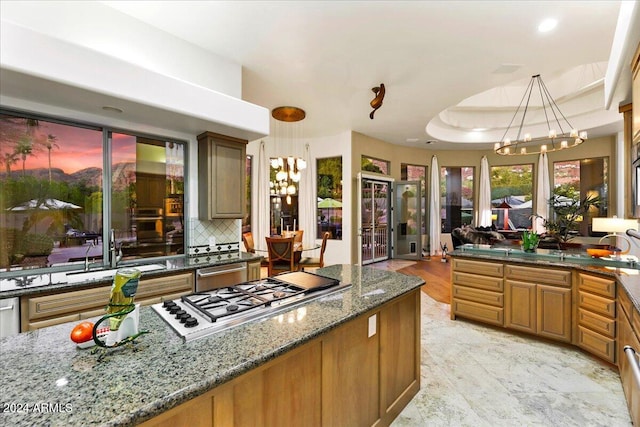 kitchen with sink, dark stone countertops, hanging light fixtures, stainless steel gas cooktop, and a raised ceiling