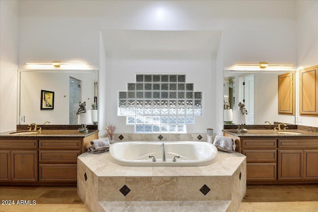 bathroom featuring tiled tub, vanity, and wood-type flooring