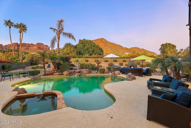 pool at dusk featuring outdoor lounge area, a mountain view, and a patio