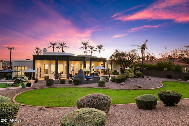 back house at dusk with a patio and a lawn