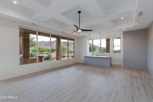 empty room featuring visible vents, a ceiling fan, a mountain view, light wood-type flooring, and coffered ceiling