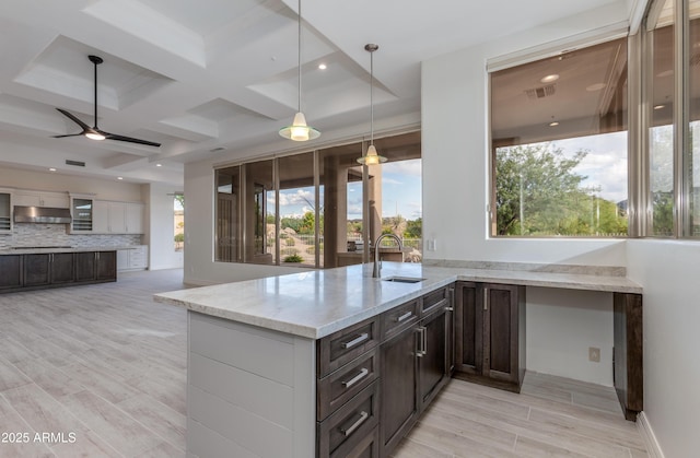 kitchen with visible vents, decorative backsplash, light stone counters, under cabinet range hood, and a sink