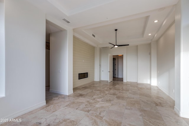 empty room with ceiling fan, a large fireplace, visible vents, baseboards, and a tray ceiling