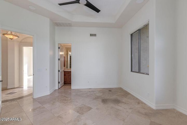 empty room with a ceiling fan, a raised ceiling, visible vents, and baseboards