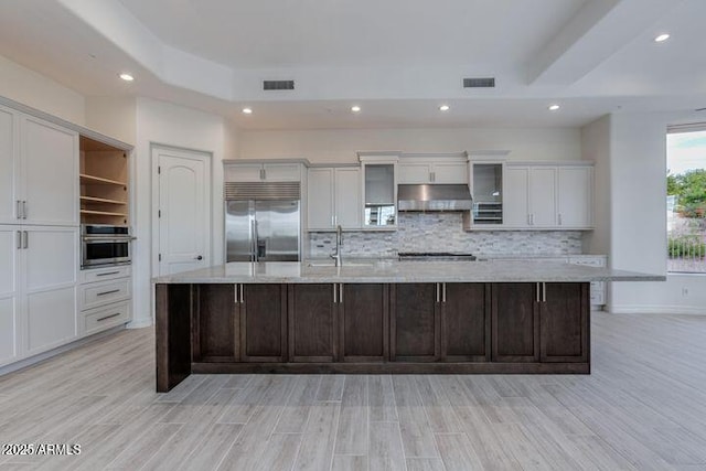 kitchen featuring a large island, visible vents, appliances with stainless steel finishes, glass insert cabinets, and under cabinet range hood