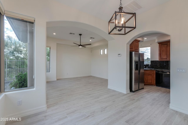 kitchen with black dishwasher, dark countertops, hanging light fixtures, brown cabinetry, and stainless steel fridge