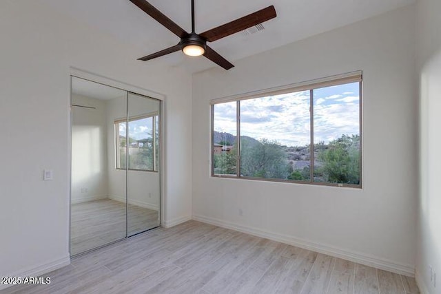 unfurnished bedroom featuring a ceiling fan, a closet, light wood-style flooring, and baseboards