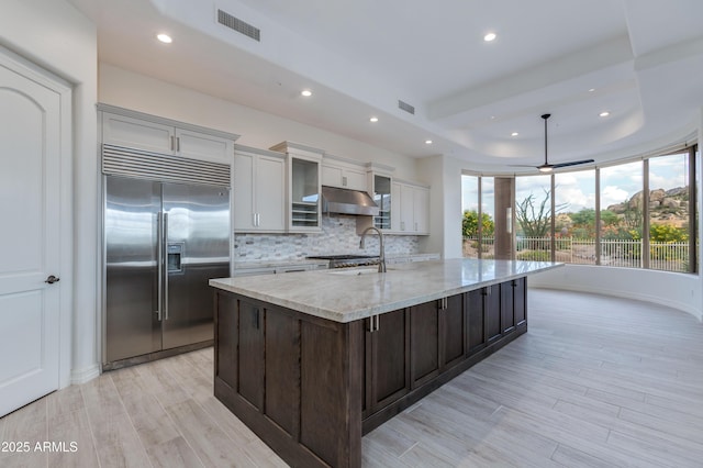 kitchen featuring light stone countertops, a kitchen island with sink, glass insert cabinets, and stainless steel appliances