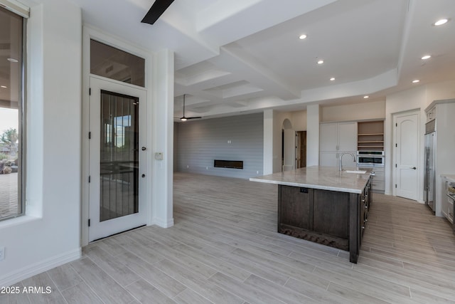 kitchen featuring dark brown cabinetry, a center island with sink, stainless steel appliances, a fireplace, and a sink