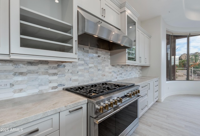 kitchen with extractor fan, white cabinets, double oven range, light stone countertops, and glass insert cabinets