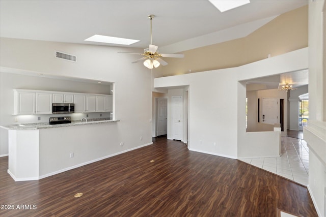 unfurnished living room featuring dark hardwood / wood-style flooring, ceiling fan with notable chandelier, a skylight, and high vaulted ceiling