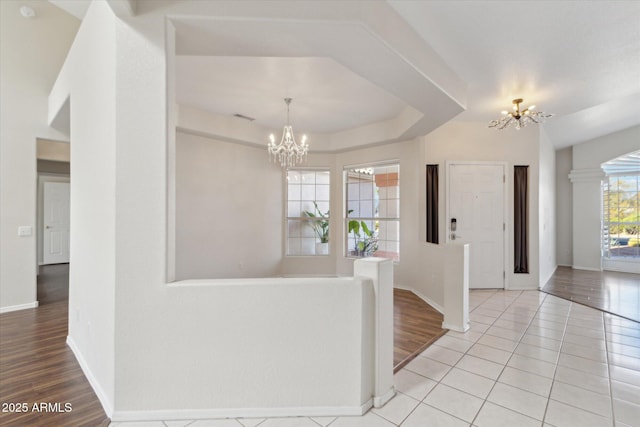 interior space with ornate columns, light tile patterned flooring, a chandelier, and a tray ceiling