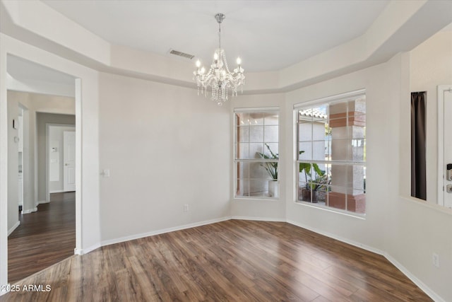 empty room featuring an inviting chandelier, dark hardwood / wood-style floors, and a raised ceiling