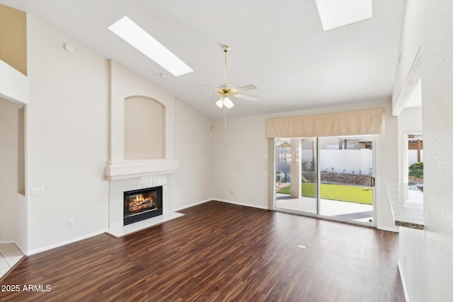 unfurnished living room with dark hardwood / wood-style floors, high vaulted ceiling, a skylight, a tiled fireplace, and ceiling fan