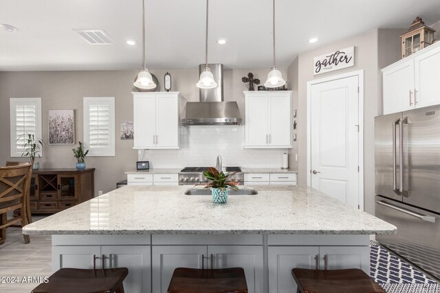 kitchen with white cabinets, light stone countertops, high quality fridge, and wall chimney range hood