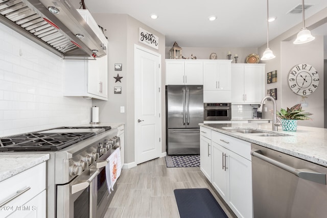 kitchen featuring light stone counters, wall chimney range hood, sink, white cabinets, and high end appliances