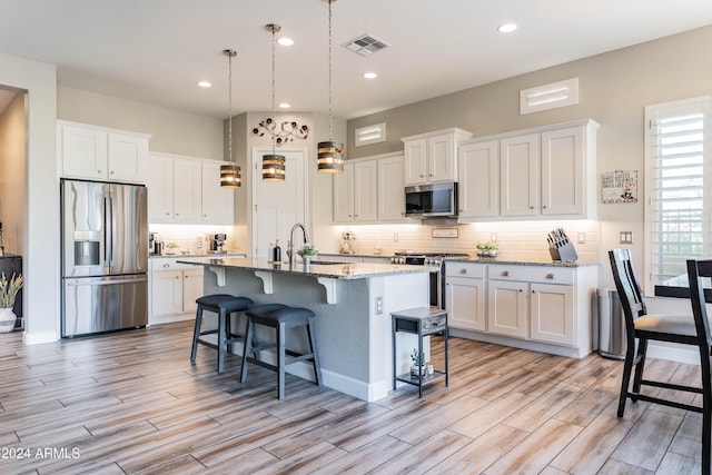 kitchen with stone counters, a breakfast bar, white cabinets, a center island with sink, and appliances with stainless steel finishes