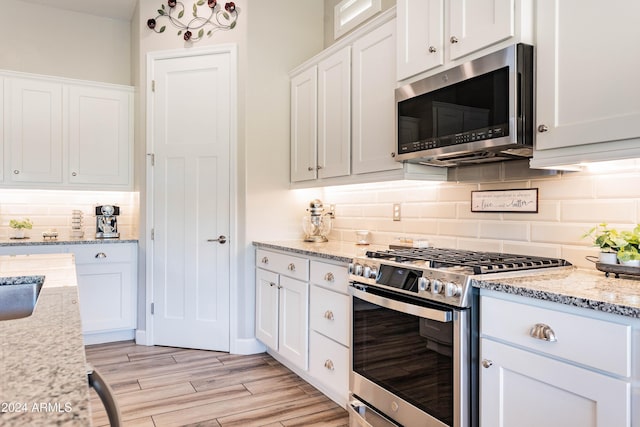 kitchen with tasteful backsplash, light stone counters, white cabinets, and stainless steel appliances