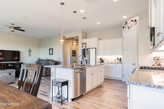 kitchen with ceiling fan, hanging light fixtures, stainless steel appliances, an island with sink, and white cabinets