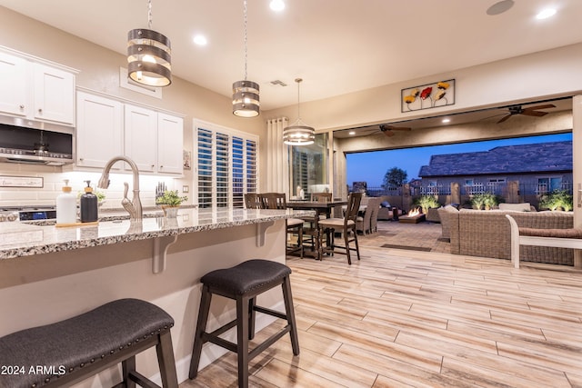 kitchen with light stone countertops, a kitchen breakfast bar, ceiling fan, decorative light fixtures, and white cabinetry