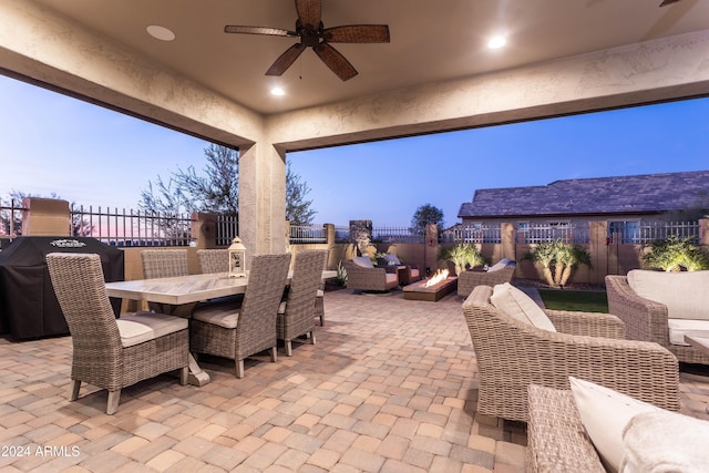 patio terrace at dusk featuring ceiling fan, area for grilling, and an outdoor living space with a fire pit