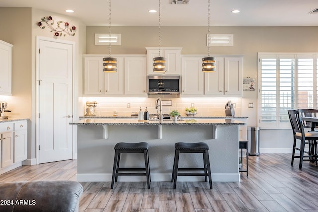 kitchen with a center island with sink, decorative backsplash, light hardwood / wood-style floors, and white cabinetry