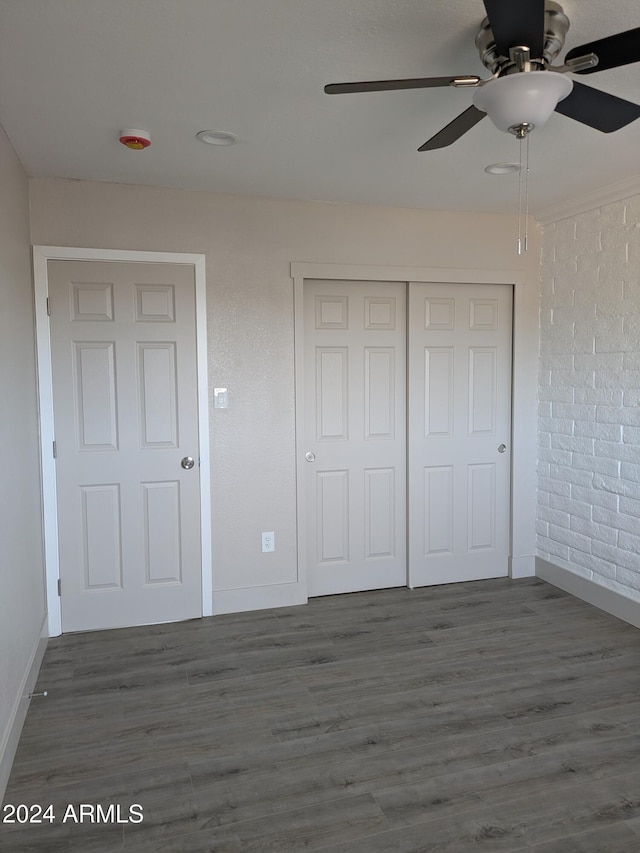 unfurnished bedroom with ceiling fan, a closet, brick wall, and dark hardwood / wood-style floors