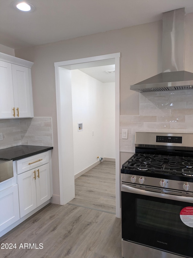 kitchen with white cabinets, wall chimney range hood, stainless steel gas stove, light wood-type flooring, and tasteful backsplash